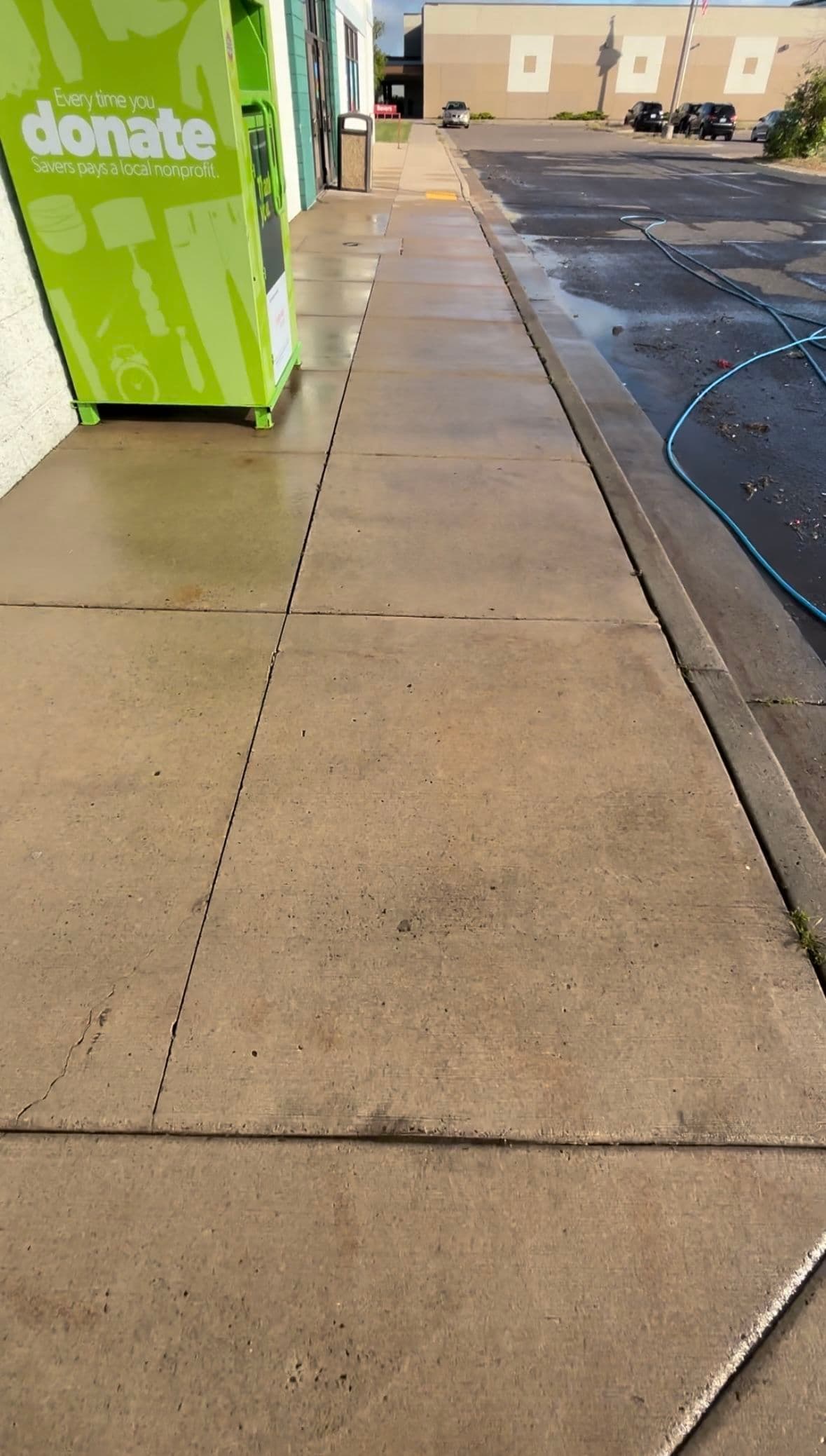 Clean sidewalk next to a donation box on a sunny day, with vehicles in the background.